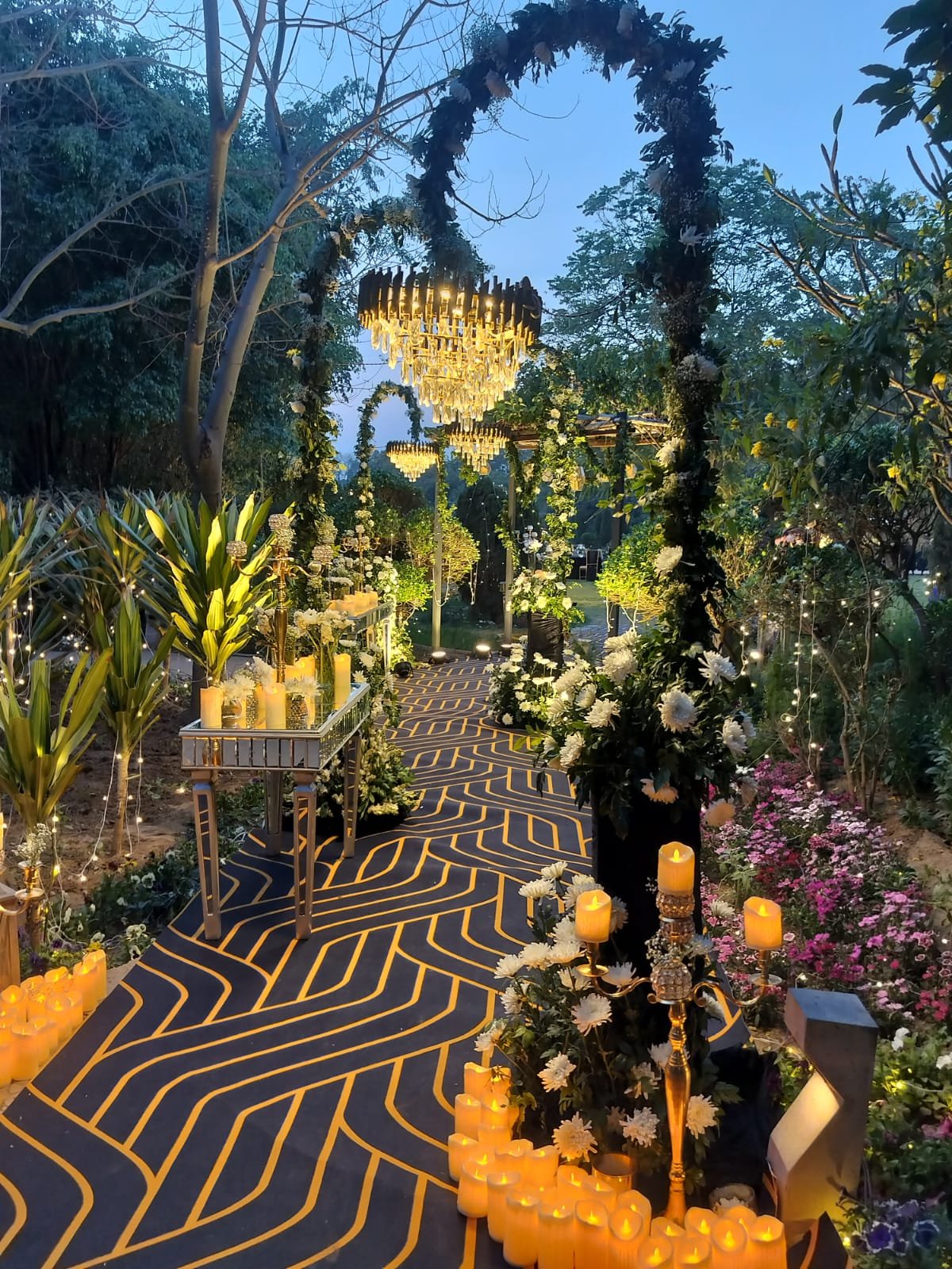 Candlelit garden walkway with chandeliers hung from the trees