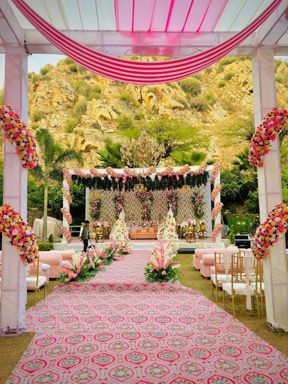 Pink floral mandap and aisle set against the hills