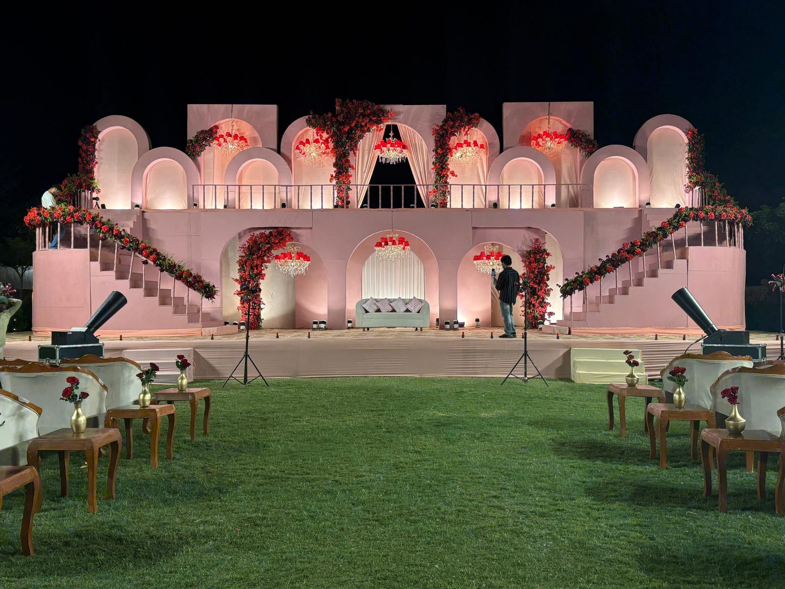 Arched wedding stage with chandeliers and red floral garlands by Royal Tales